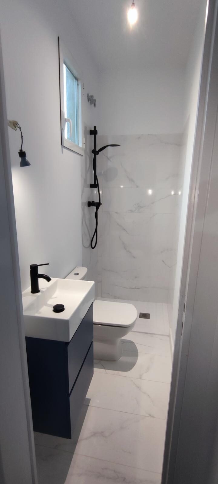 Baño terminado con porcelánico efecto mármol, ducha a ras y grifería negra