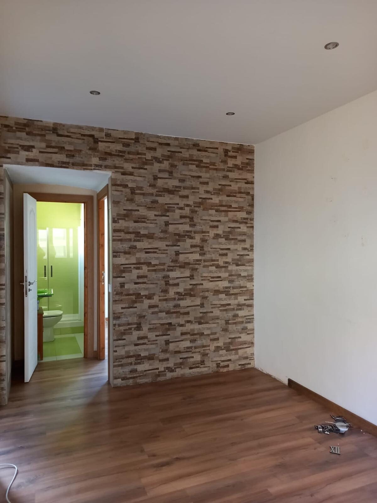 Dormitorio reformado con pared de piedra decorativa, suelo laminado y baño en suite