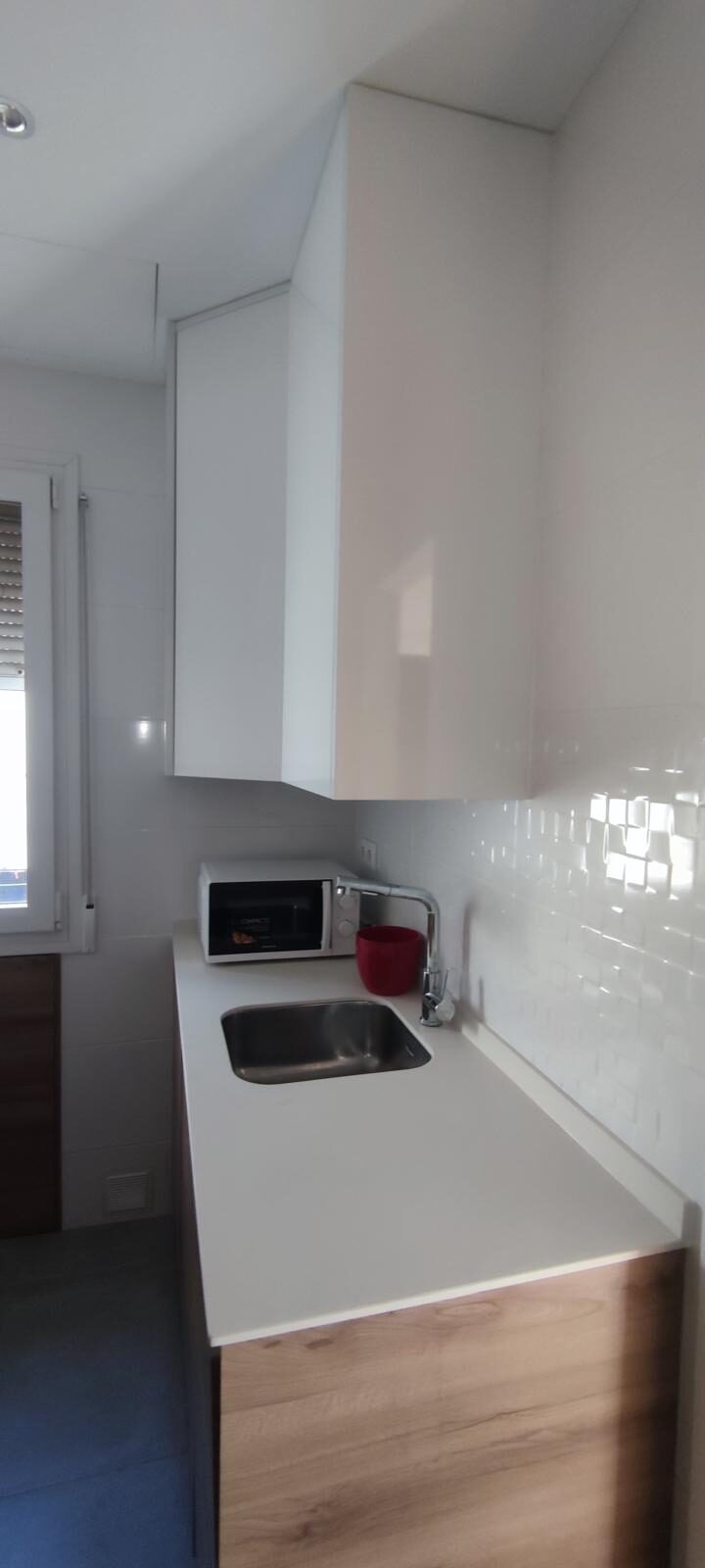 Cocina alargada terminada con muebles blancos en brillo y encimera continua