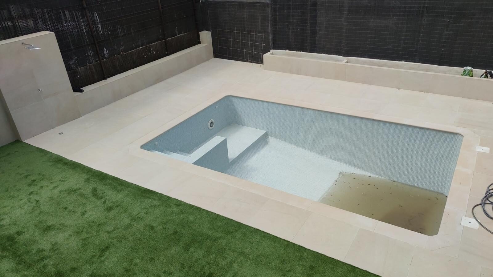 Piscina reformada con pavimento beige, ducha exterior y gresite nuevo
