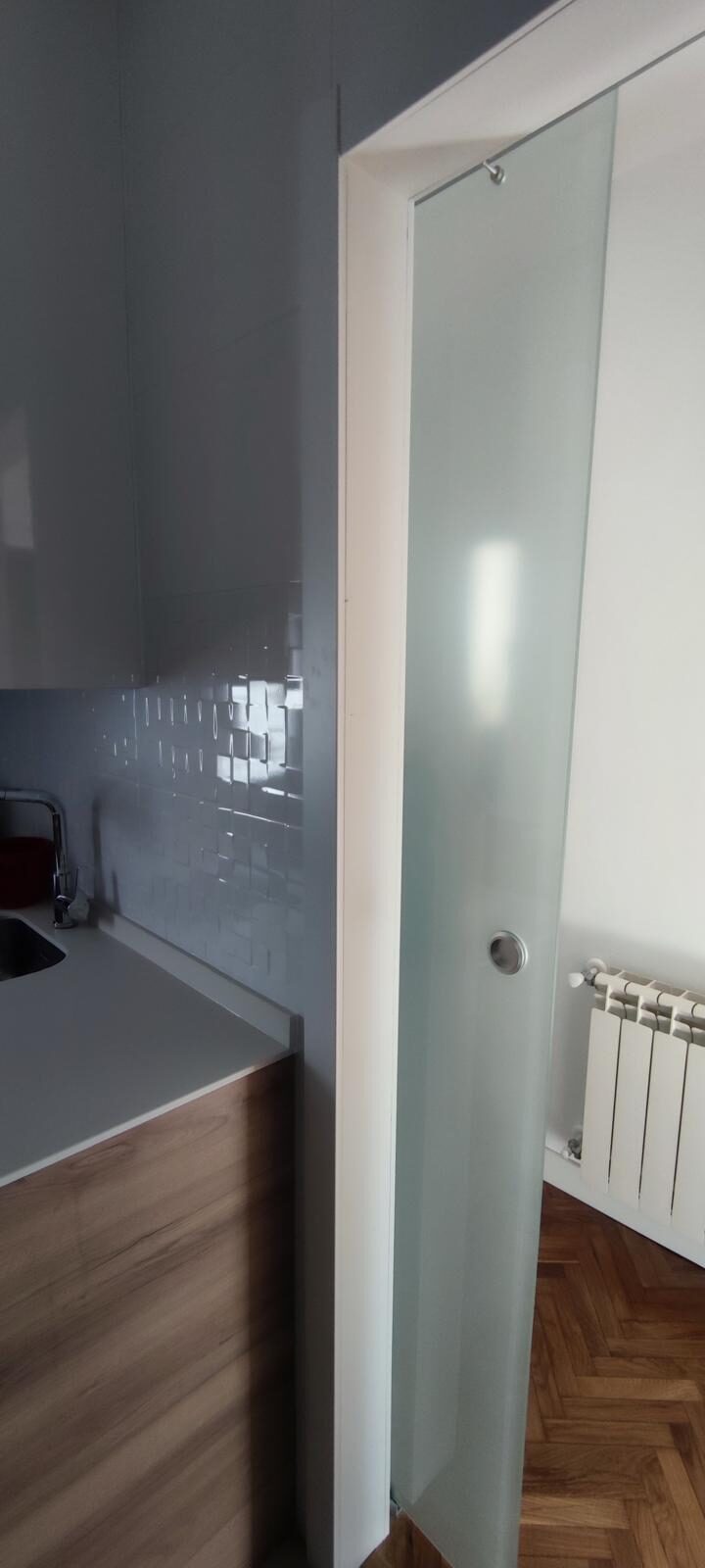 Detalle de cocina con frente de azulejo metro blanco, encimera continua y puerta corredera de cristal