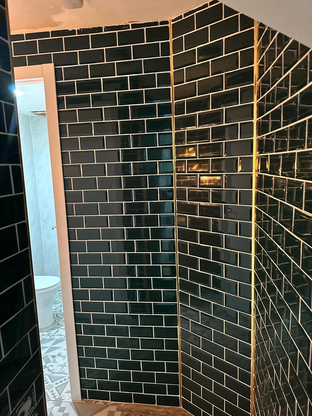 Pasillo de aseos alicatado con azulejo metro negro y remates dorados