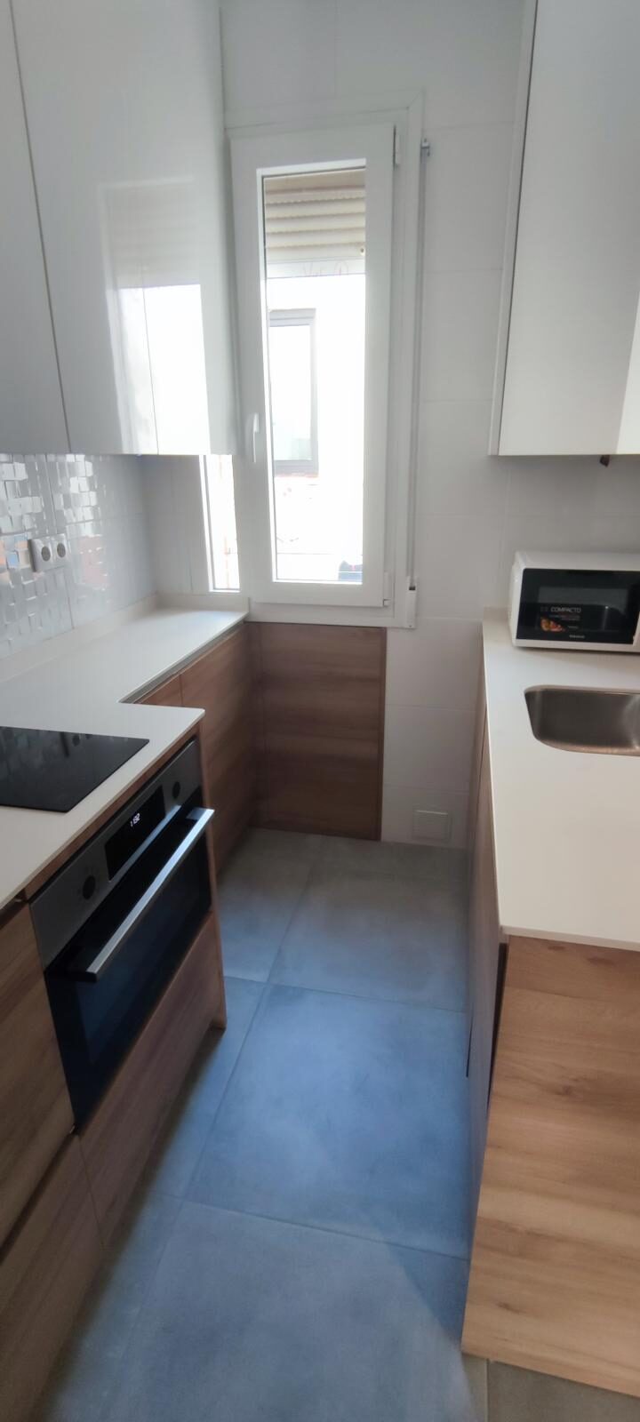 Cocina terminada con mobiliario blanco y madera, encimera continua y electrodomésticos integrados