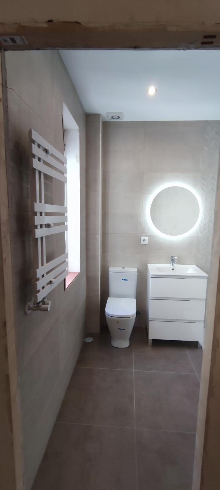 Baño terminado en blanco con espejo redondo retroiluminado y mueble suspendido